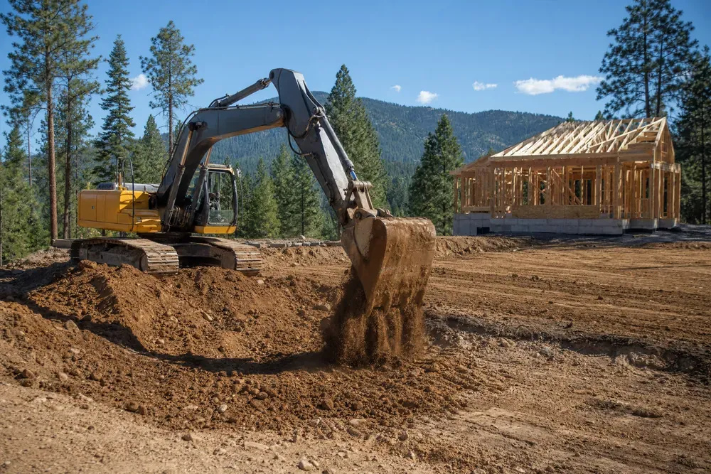 Excavator grading a residential building pad on a North Idaho site